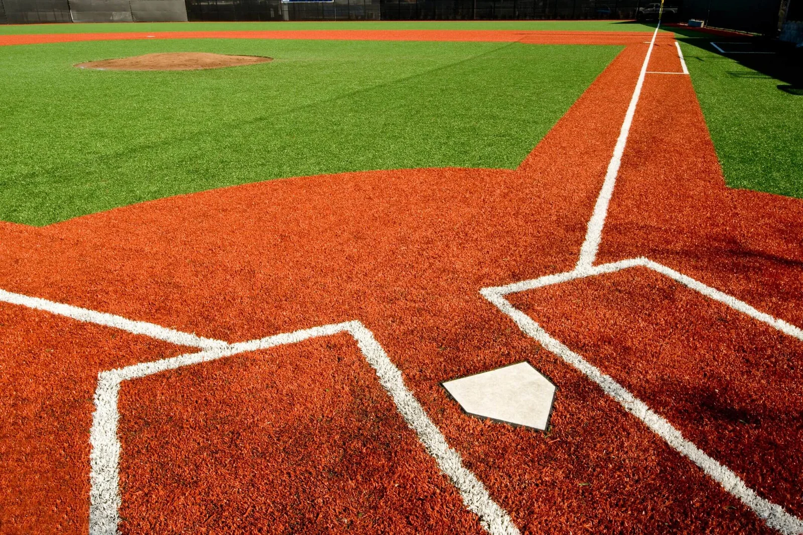 A close-up view of a baseball field’s home plate area in El Mirage, with bright orange artificial turf expertly laid by professional artificial turf installers, crisp white baselines, and the pitcher’s mound visible under bright sunlight.