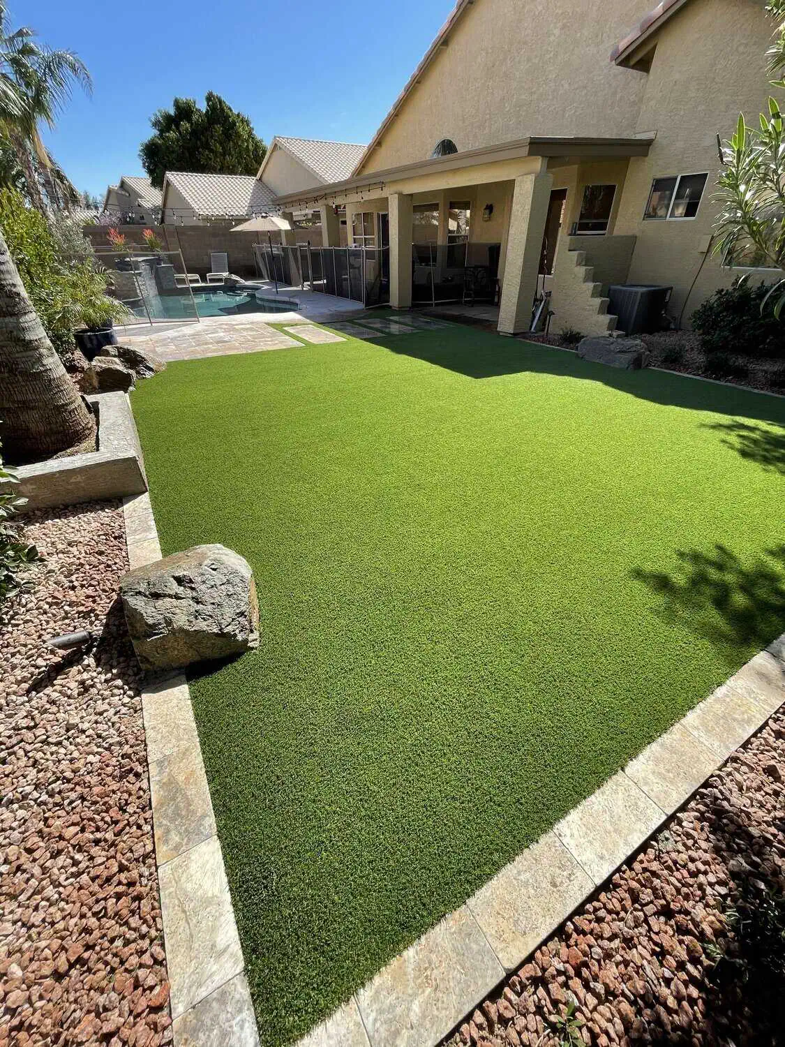 A single brown leaf with visible veins lies on a well-manicured, lush green artificial grass installation in Peoria, Arizona. The contrast between the brown leaf and the vibrant green grass highlights the leaf's texture and detailed structure. Contact us for a free quote today!
